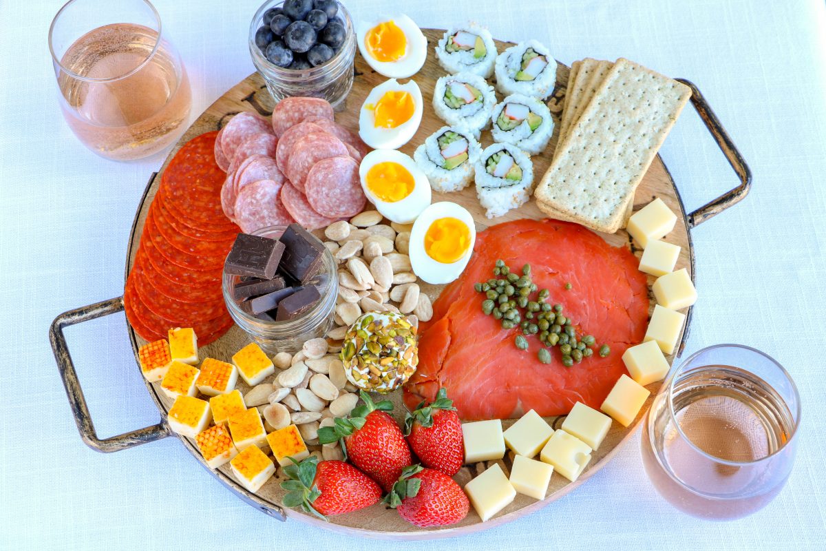 charcuterie board with assorted cheeses, meats, soft boiled eggs, salmon and berries